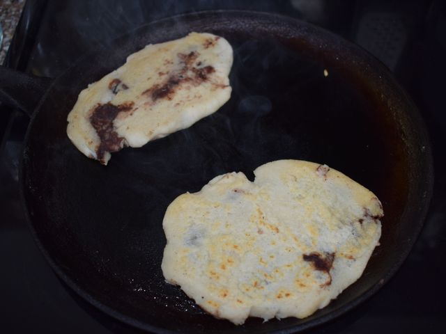 image of pupusas cooking on cast iron skillet leaking some beans