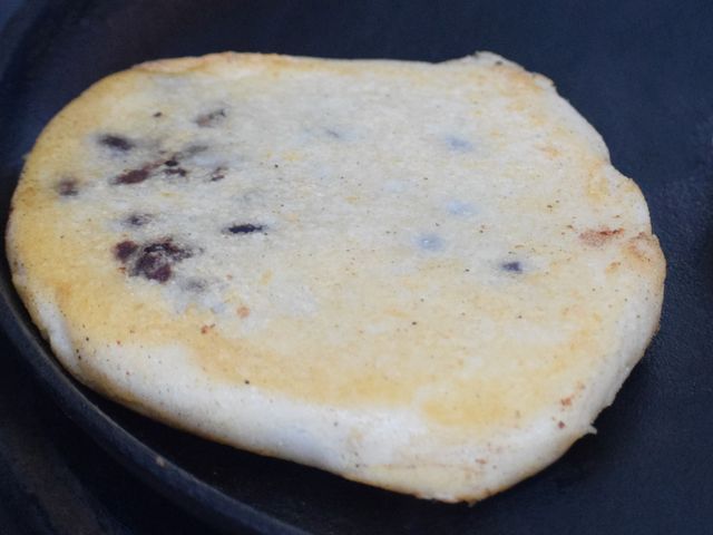 image of a pupusa cooking on cast iron skillet after leaking some beans
